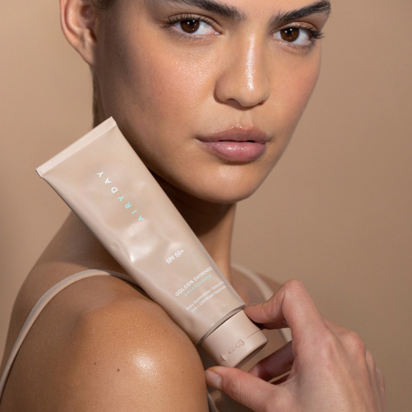 Woman holding a tube of Airyday  sunscreen against a beige background